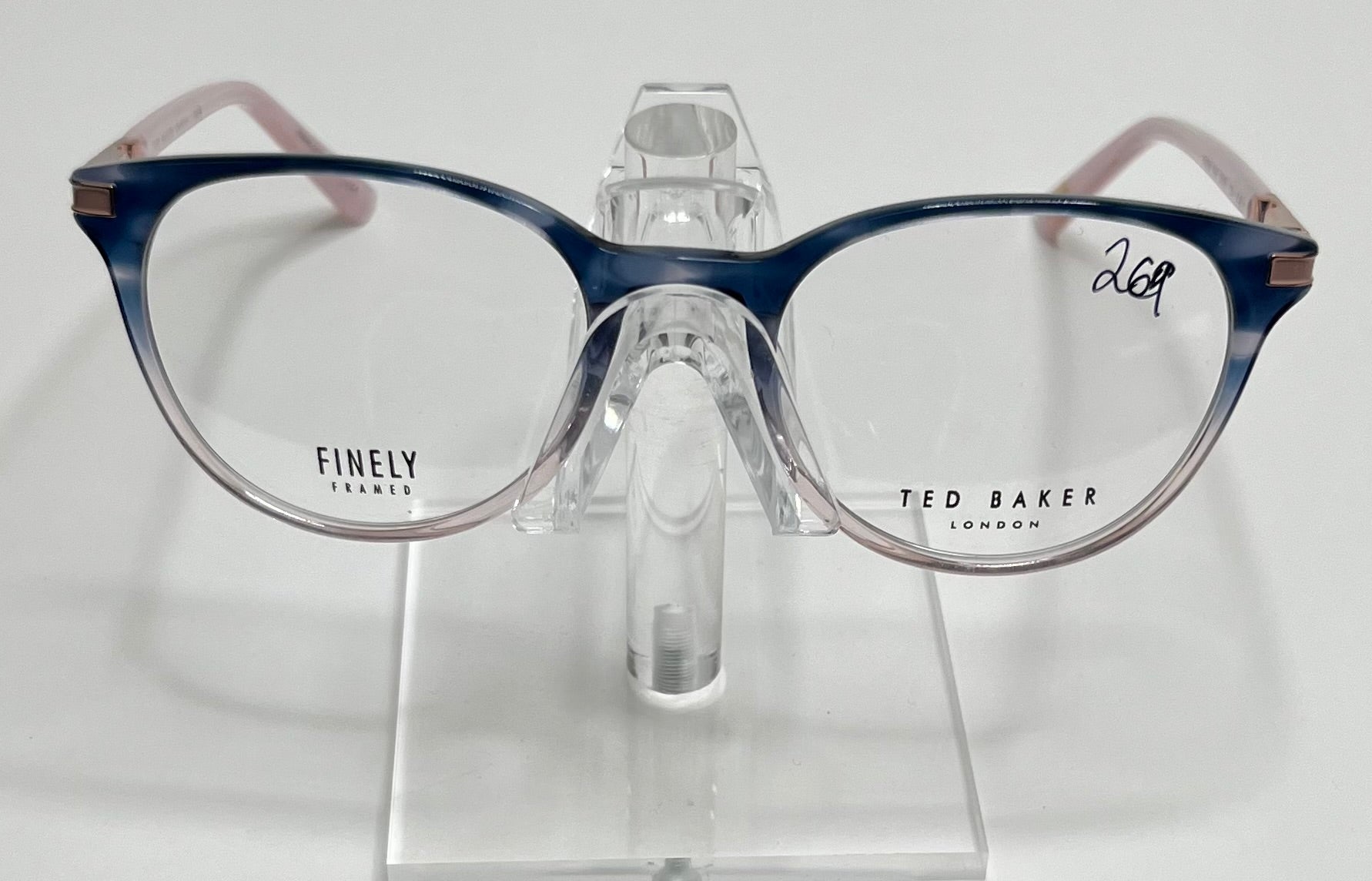 A pair of Ted Baker TFW006 ladies eyeglass frames in navy and pink color displayed on a stand.