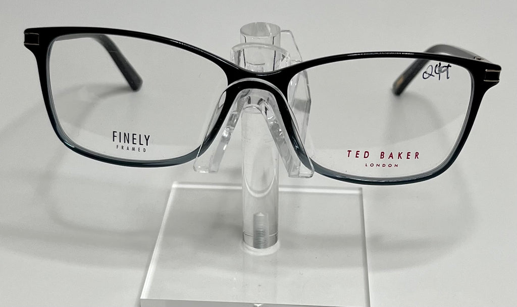 A pair of Ted Baker TFW004 eyeglasses with black and blue frames, displayed on a stand.