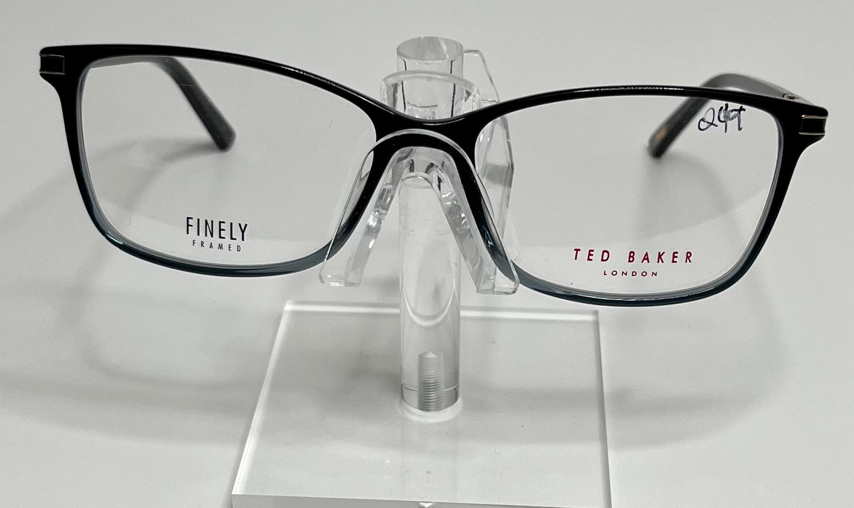A pair of Ted Baker TFW004 eyeglasses with black and blue frames, displayed on a stand.