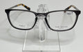 A pair of Ted Baker TFM004 men's eyeglasses with a sleek gray front and tortoise temples displayed on a stand.
