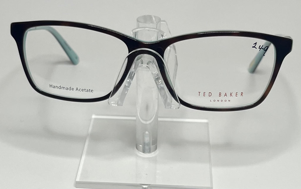 A pair of Ted Baker B740 plastic eyeglass frames in blue and tortoise colors, displayed on a stand.