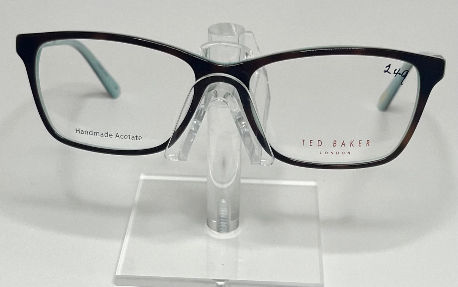 A pair of Ted Baker B740 plastic eyeglass frames in blue and tortoise colors, displayed on a stand.
