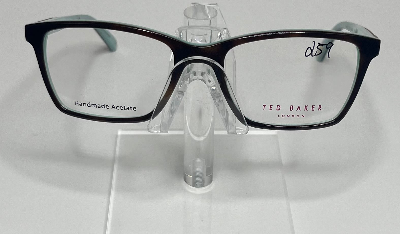 A pair of Ted Baker brand eyeglasses with a red and tortoise color scheme, displayed on a clear stand.