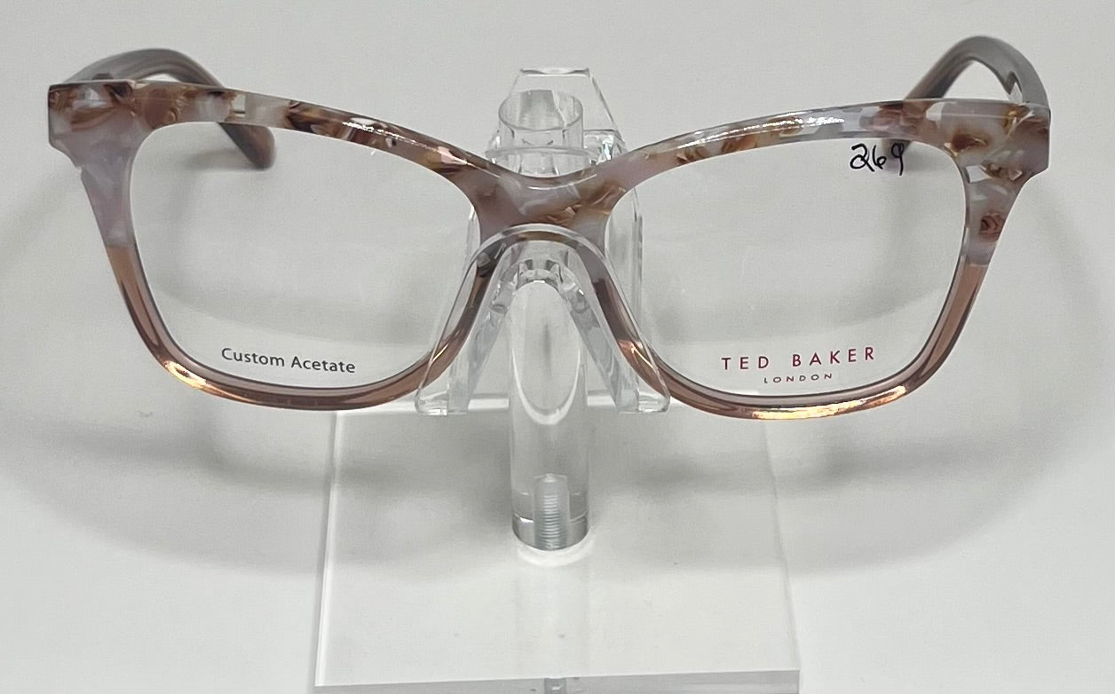 A pair of Ted Baker eyeglasses with transparent pink frames on a display stand.