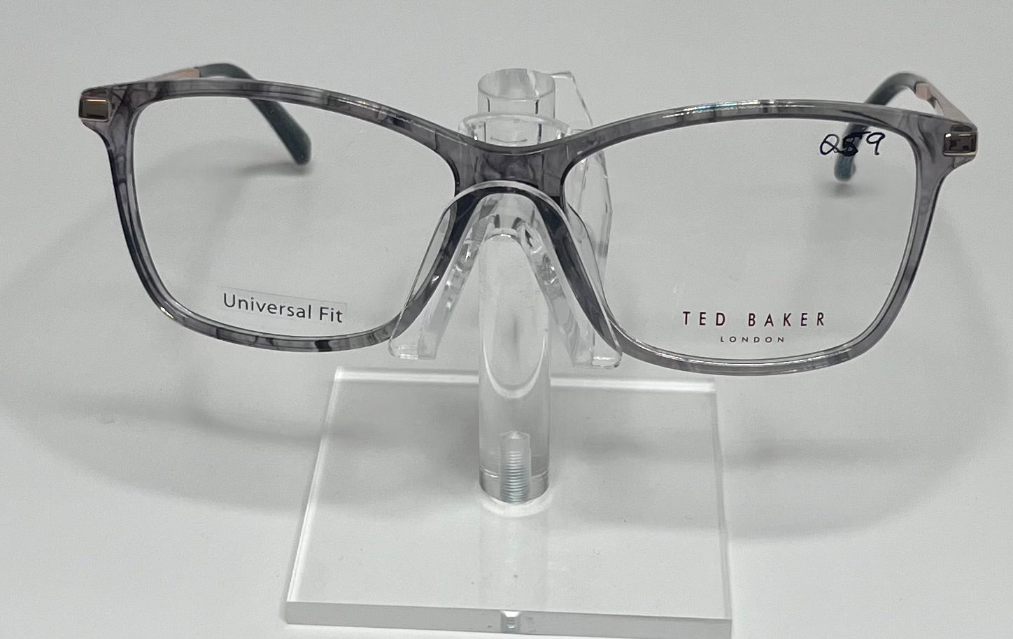 A pair of Ted Baker eyeglasses with a gray plastic frame, displayed on a stand.