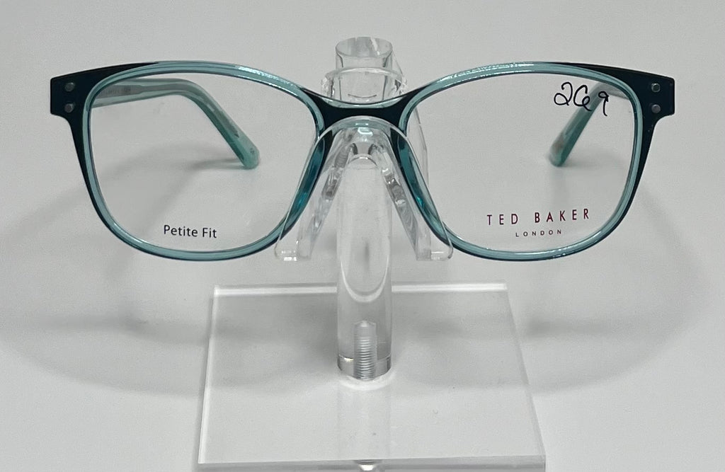 A pair of Ted Baker TPW001 eyeglasses with transparent sea green frames displayed on a stand.