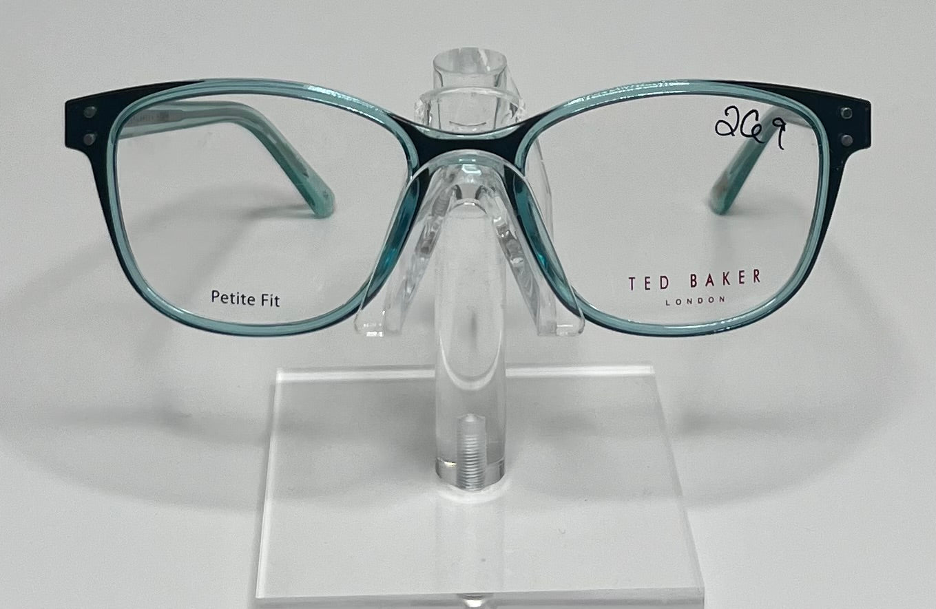 A pair of Ted Baker TPW001 eyeglasses with transparent sea green frames displayed on a stand.