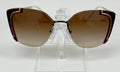 A pair of Prada sunglasses with brown gradient lenses and metallic frames on a display stand.