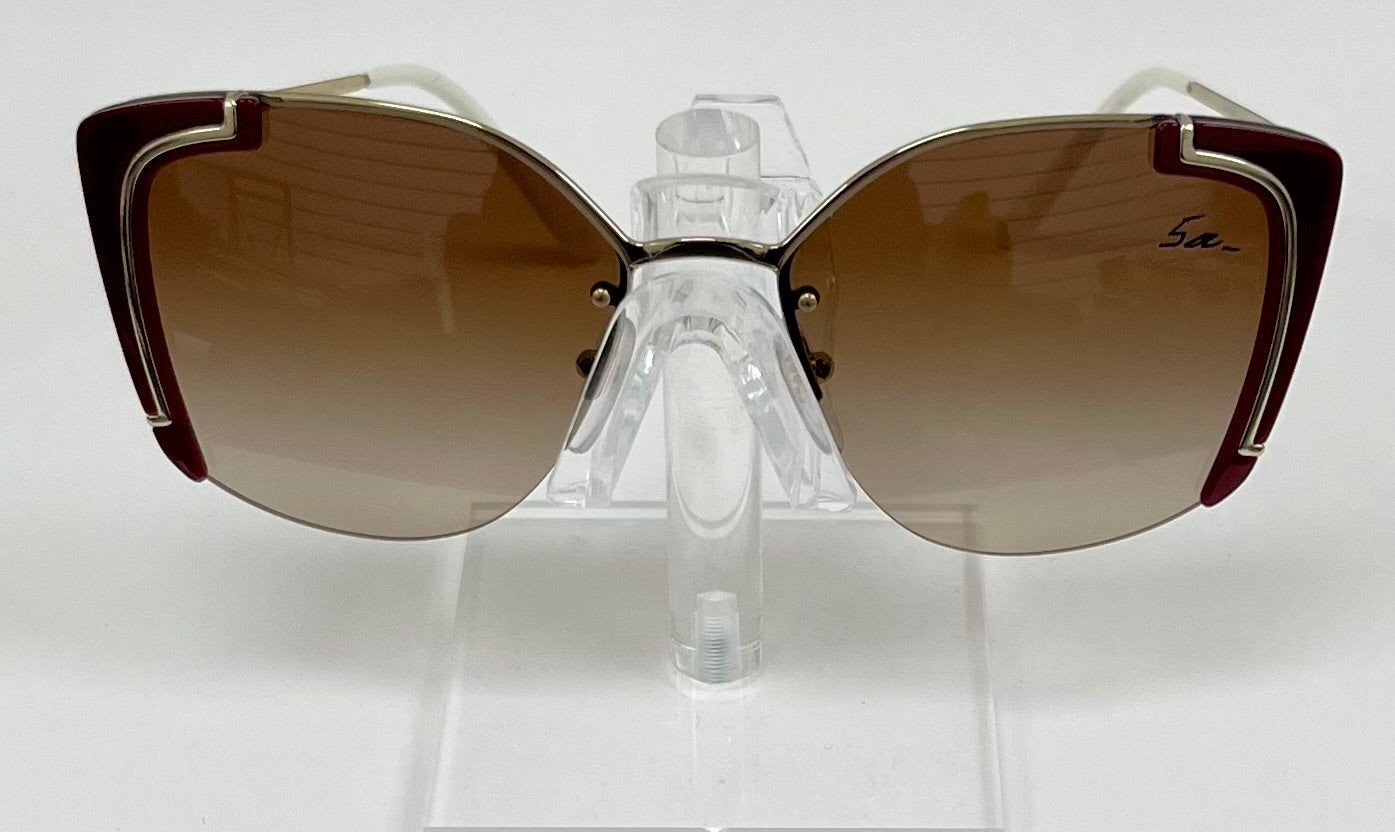 A pair of Prada sunglasses with brown gradient lenses and metallic frames on a display stand.
