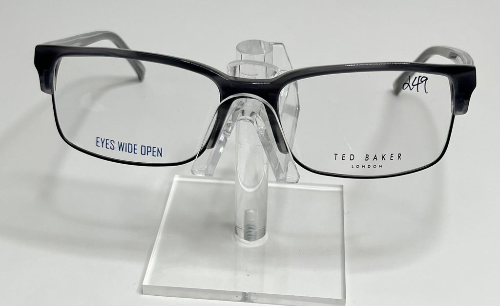 A pair of Ted Baker B347 men's eyeglasses with a black plastic frame and metal accents displayed on a stand.