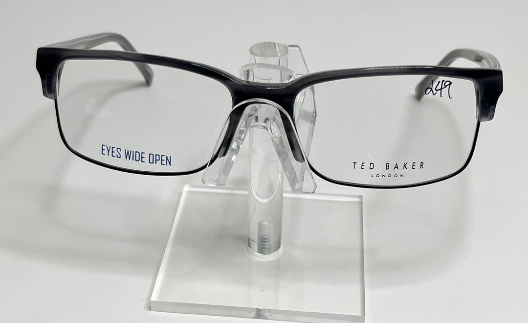 A pair of Ted Baker B347 men's eyeglasses with a black plastic frame and metal accents displayed on a stand.