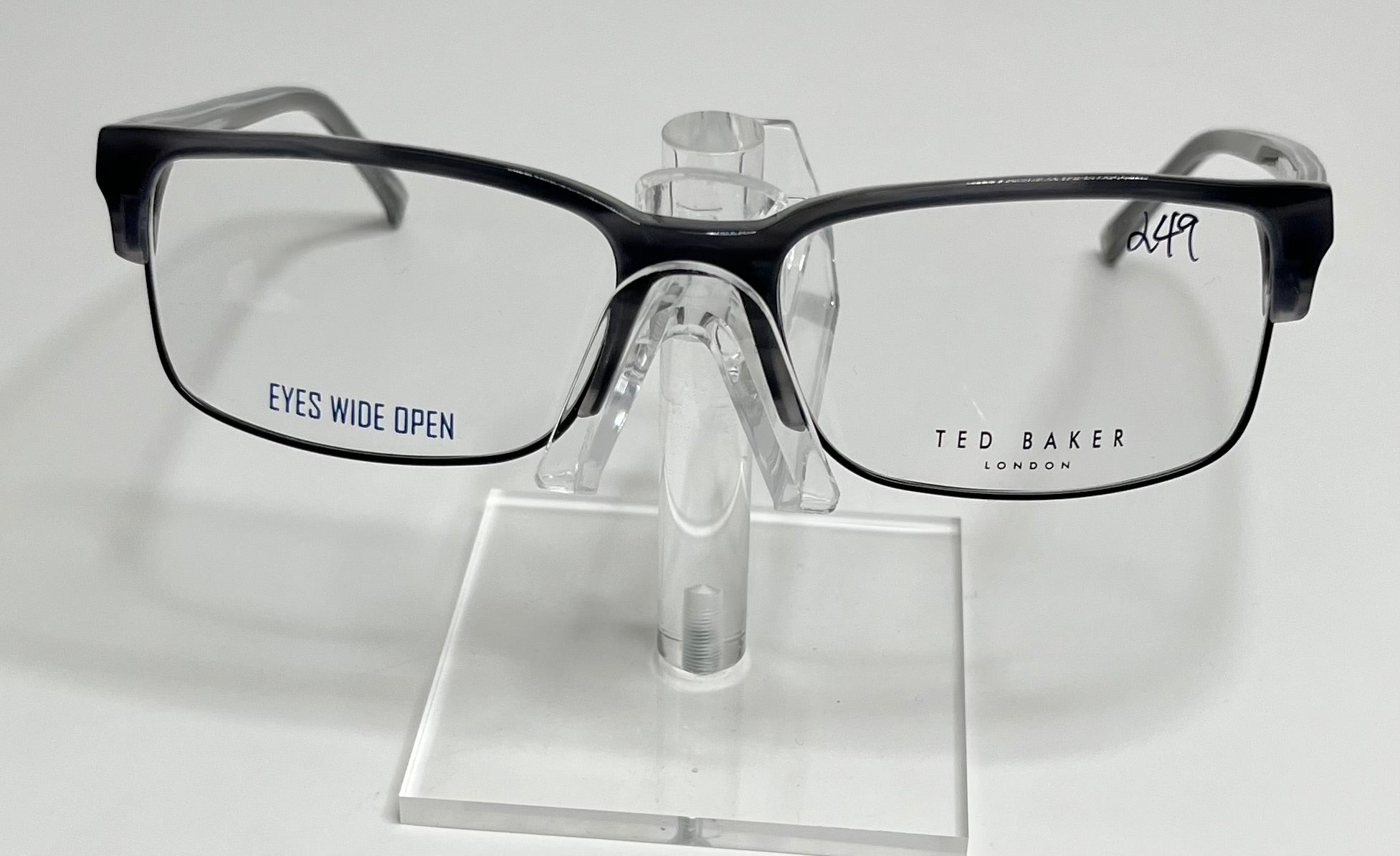 A pair of Ted Baker B347 men's eyeglasses with a black plastic frame and metal accents displayed on a stand.