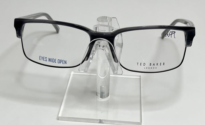 A pair of Ted Baker B347 men's eyeglasses with a black plastic frame and metal accents displayed on a stand.