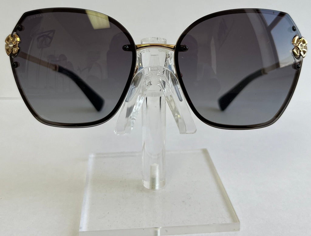 Sunglasses with gold accents on a clear stand against a white background