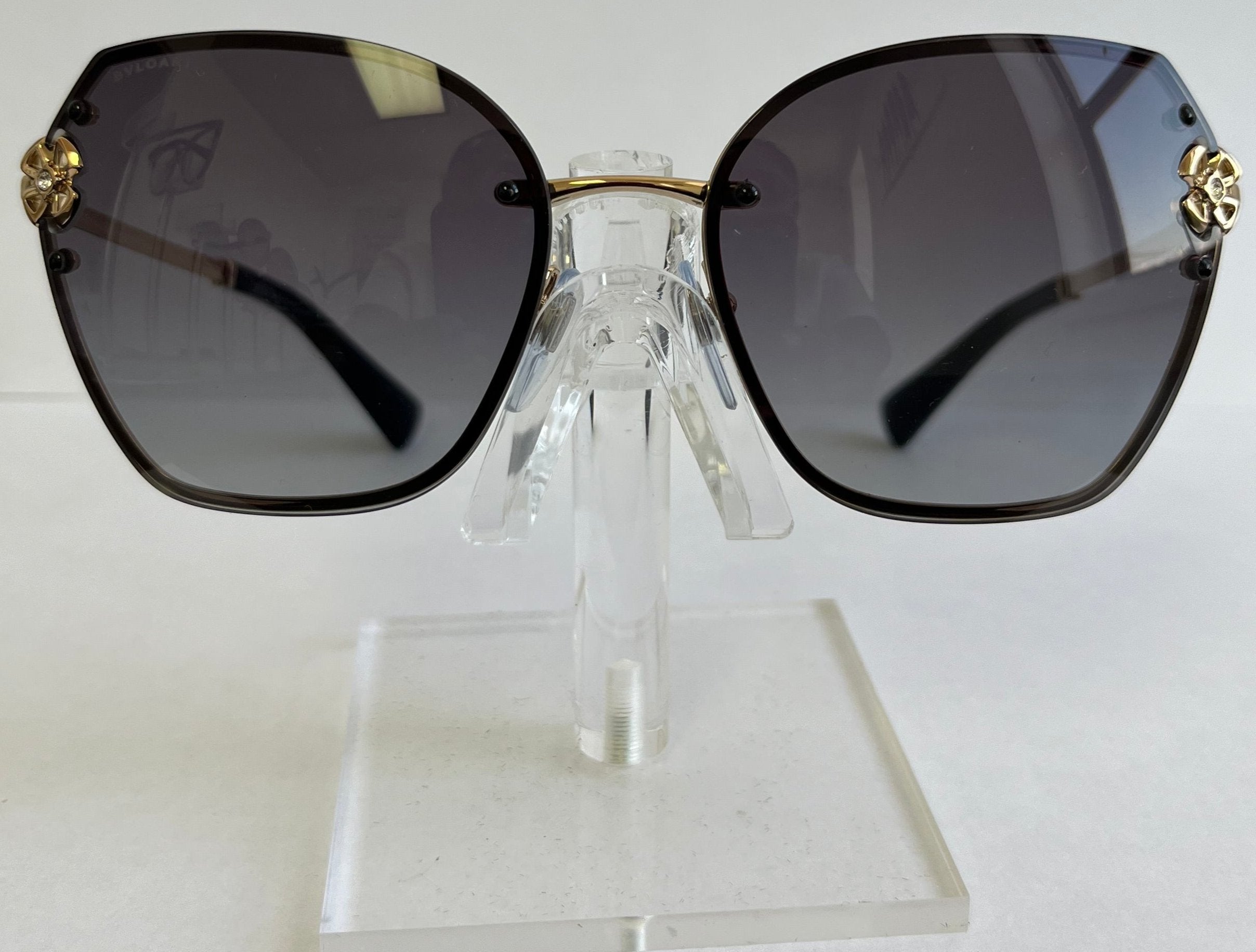 Sunglasses with gold accents on a clear stand against a white background