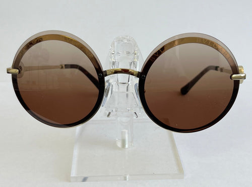 Round sunglasses with gold frames and brown lenses on a clear stand against a white background